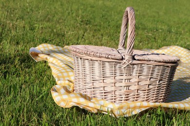 Picnic basket with checkered tablecloth on green grass outdoors, space for text