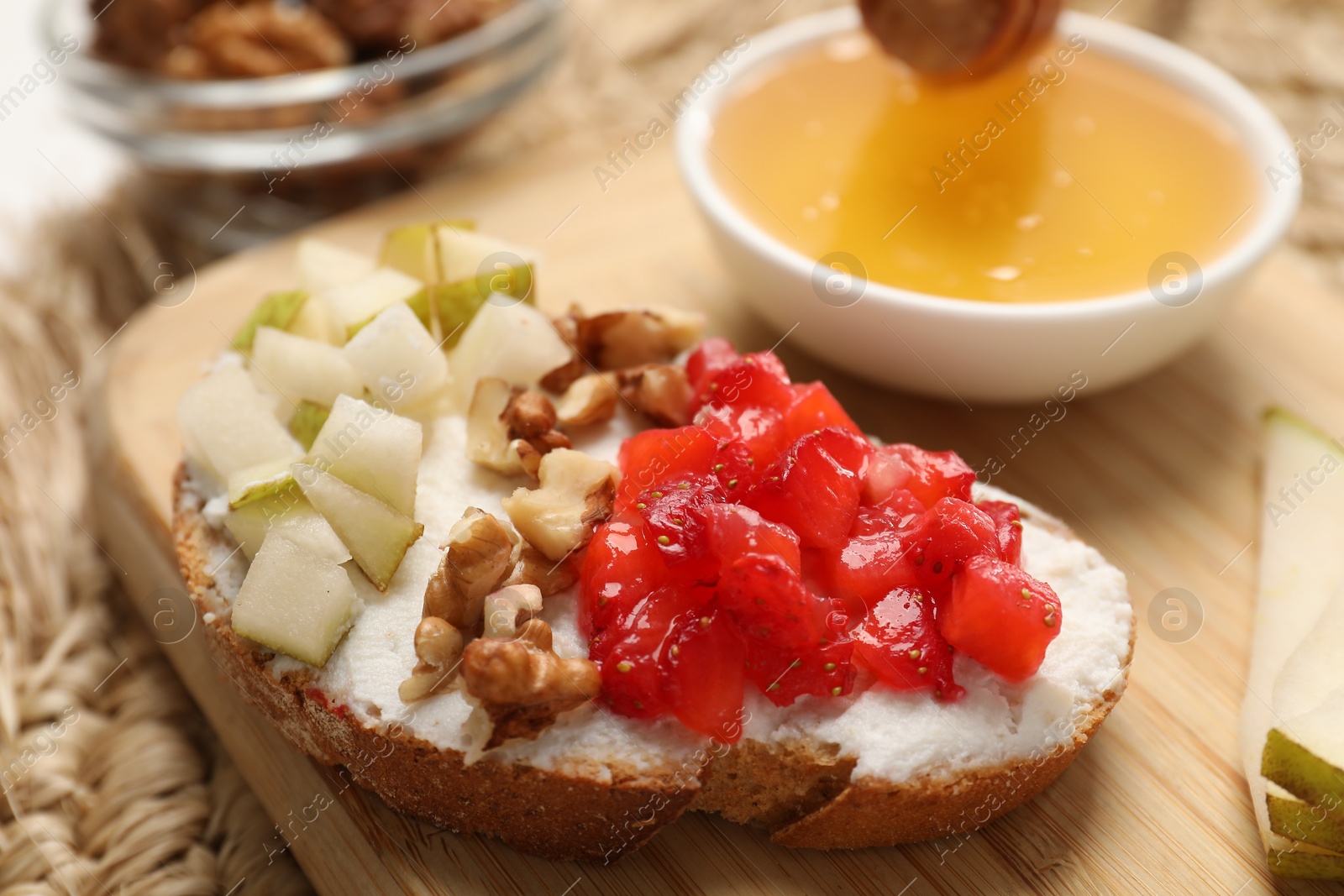 Photo of Delicious ricotta bruschetta with pear, strawberry and walnut on wooden table, closeup