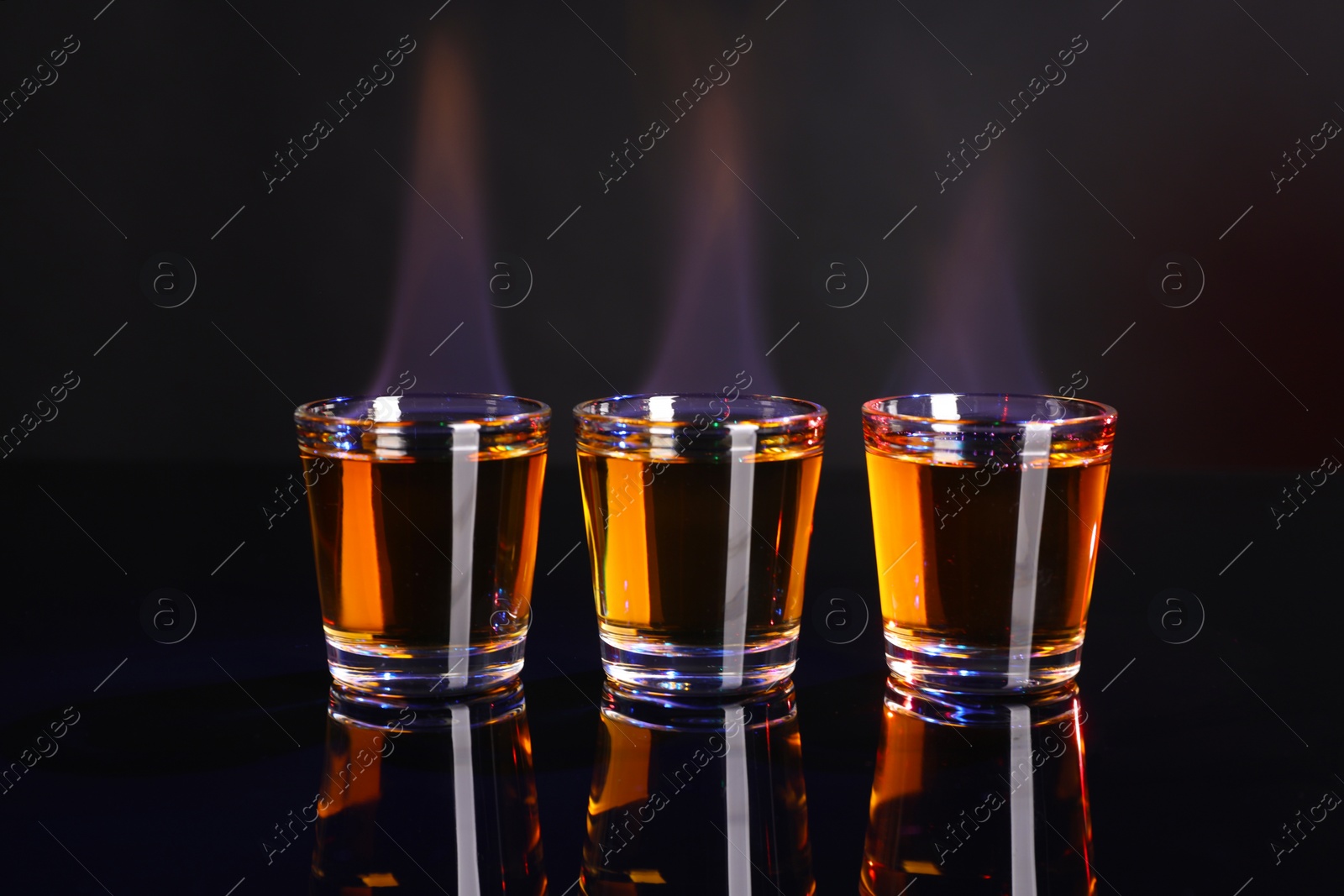 Photo of Flaming alcohol drink in shot glasses on mirror surface