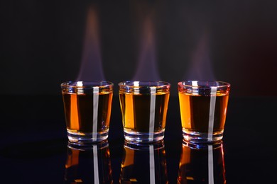 Flaming alcohol drink in shot glasses on mirror surface