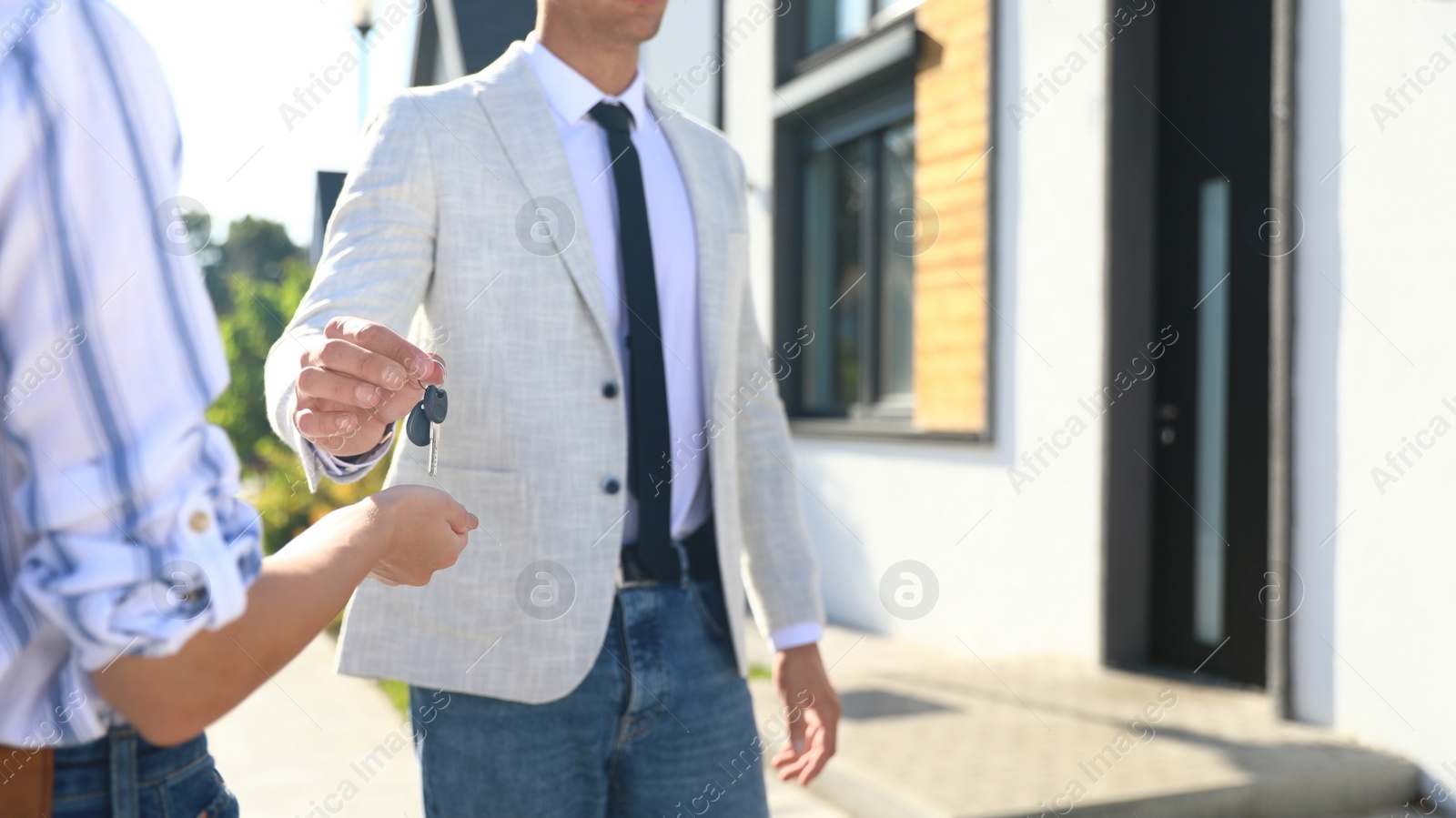 Photo of Real estate agent giving house keys to young woman outdoors, closeup