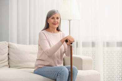 Mature woman with walking cane on sofa at home