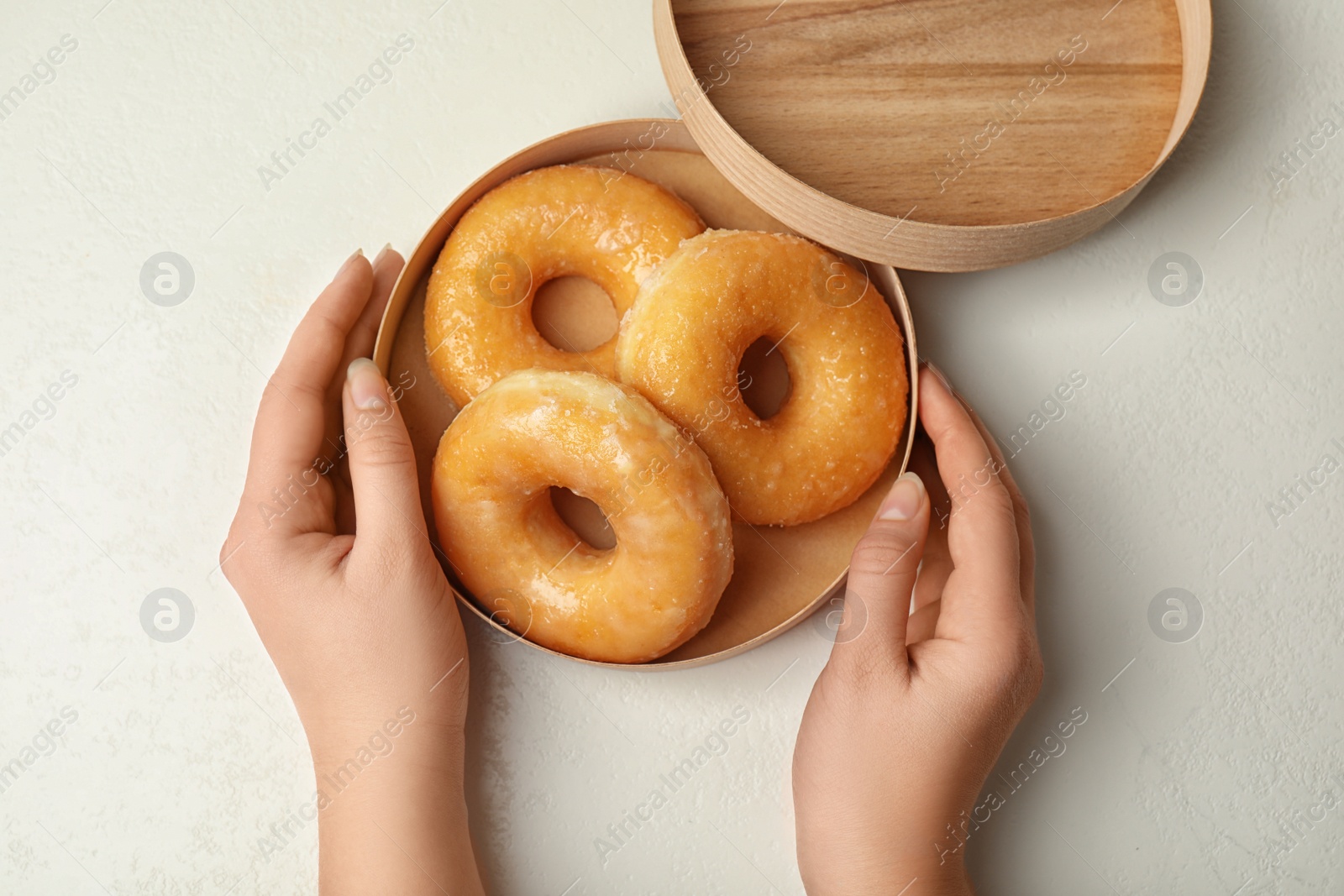 Photo of Woman with box of delicious donuts at white table, top view