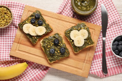 Photo of Toasts with tasty pistachio butter, banana slices, blueberries and nuts on white wooden table, flat lay
