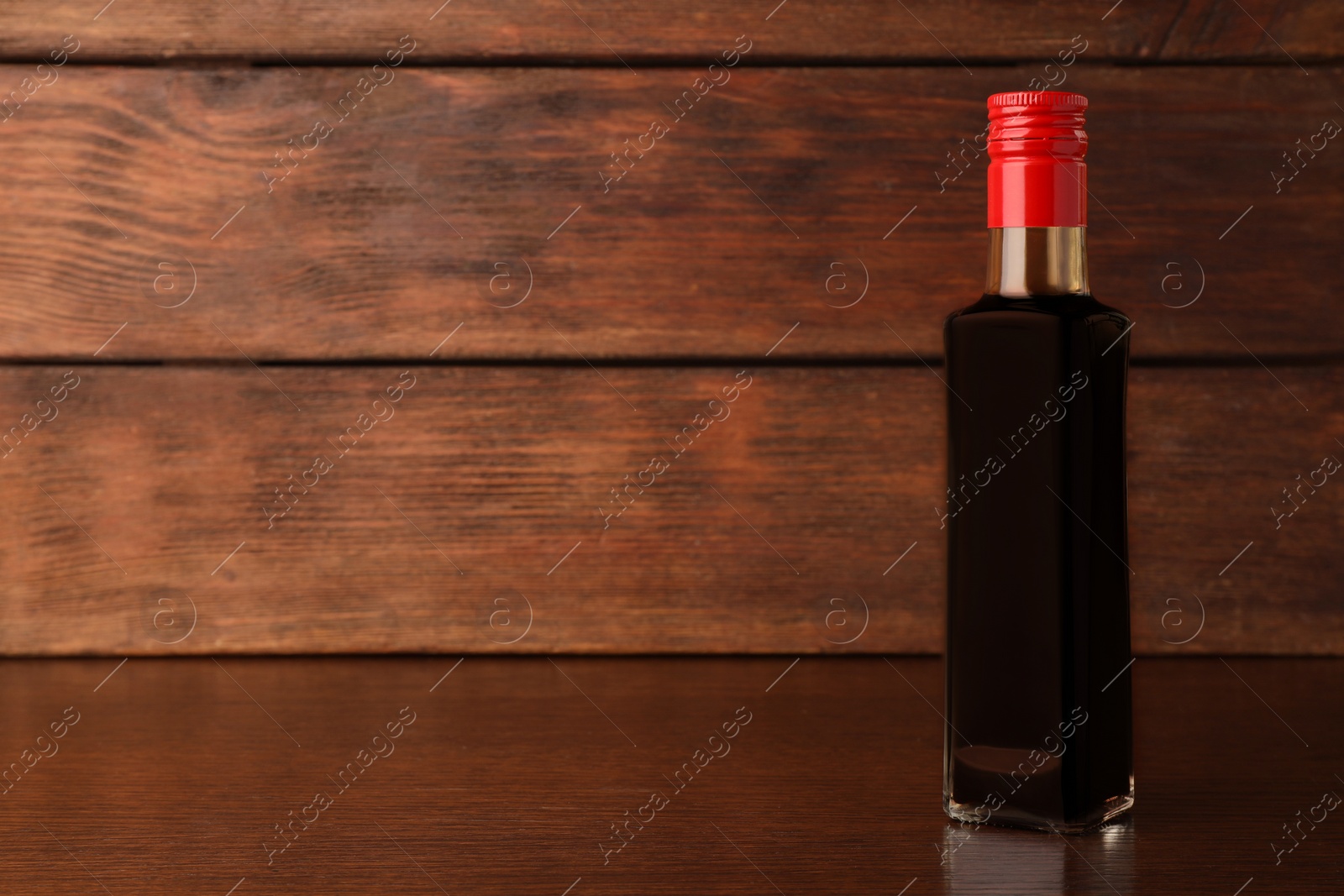 Photo of Bottle of soy sauce on wooden table. Space for text