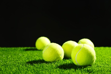 Photo of Tennis balls on green grass against dark background. Space for text