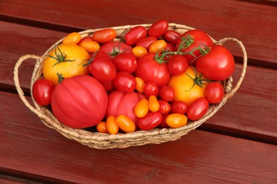Photo of Wicker basket with fresh tomatoes on wooden table, above view