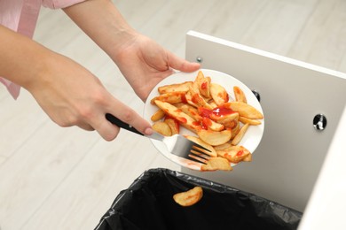 Woman throwing baked potato with ketchup into bin indoors, closeup