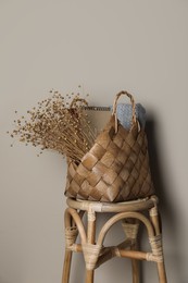 Stylish straw bag with beautiful dried flowers on chair near grey wall