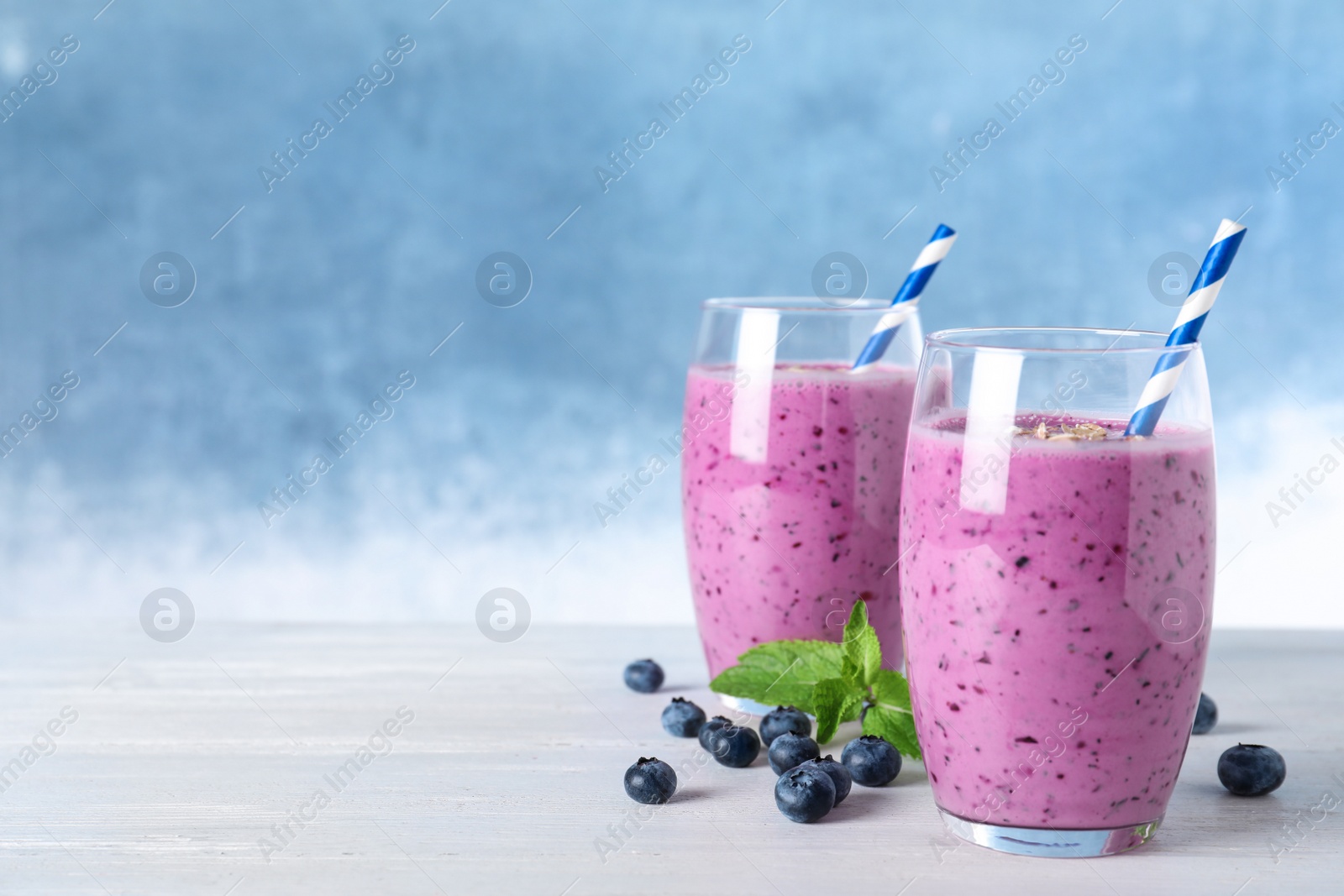 Photo of Glasses of tasty blueberry smoothie on white wooden table, space for text