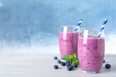 Glasses of tasty blueberry smoothie on white wooden table, space for text