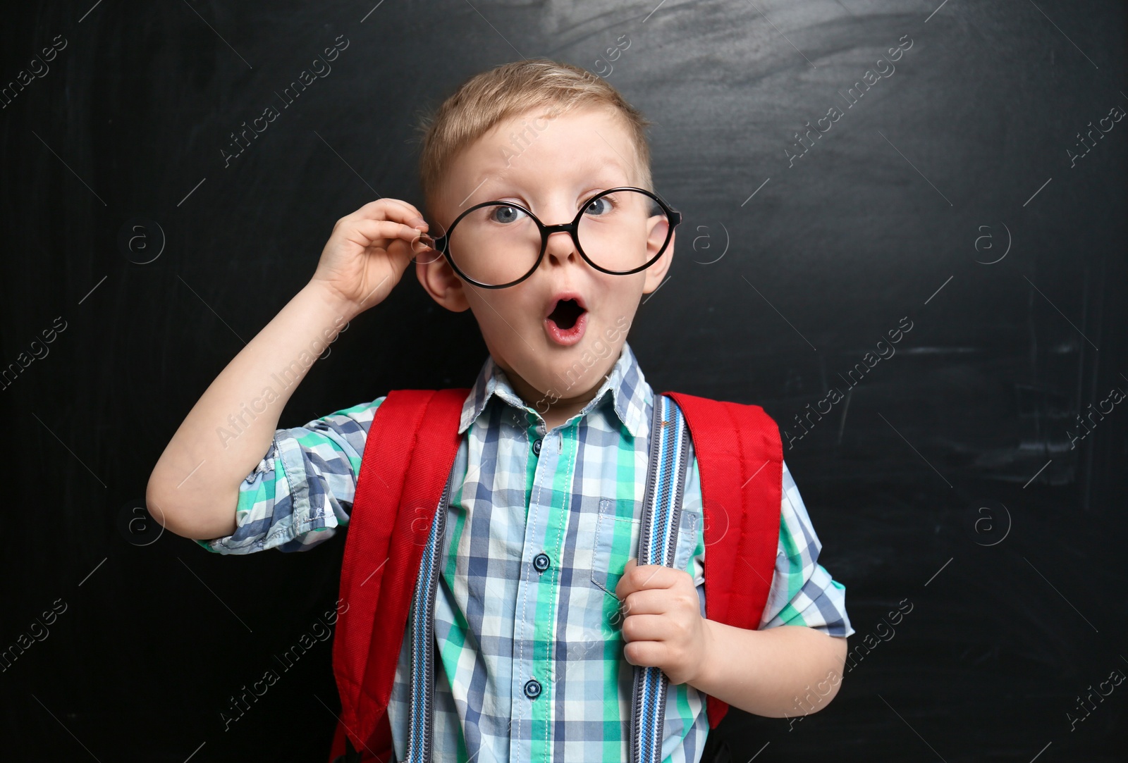 Photo of Funny little child wearing glasses near chalkboard. First time at school