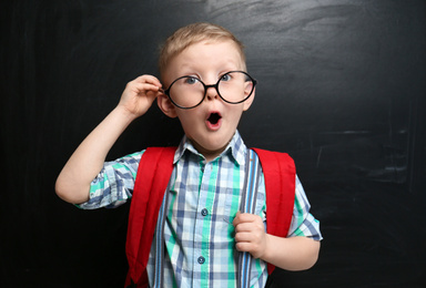 Photo of Funny little child wearing glasses near chalkboard. First time at school