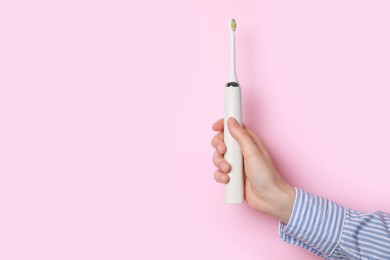 Photo of Woman holding electric toothbrush on pink background, closeup