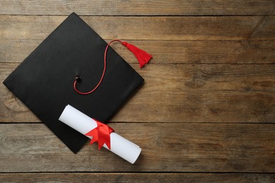 Graduation hat and diploma on wooden table, flat lay. Space for text