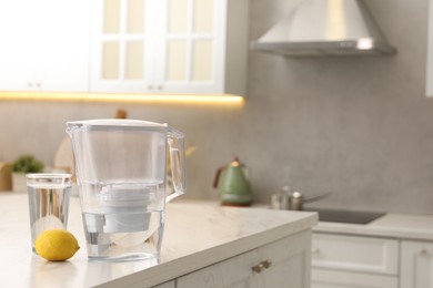 Photo of Water filter jug, glass and lemon on white marble table in kitchen, space for text