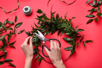 Photo of Florist making beautiful mistletoe wreath on red background, top view. Traditional Christmas decor