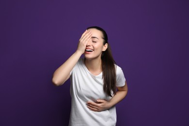 Beautiful young woman laughing on purple background. Funny joke