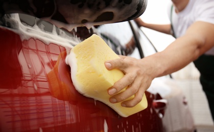 Photo of Male worker cleaning vehicle with sponge at car wash