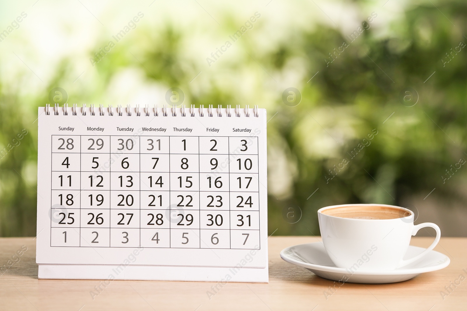 Photo of Calendar and cup of coffee on wooden table against blurred background