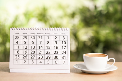 Photo of Calendar and cup of coffee on wooden table against blurred background