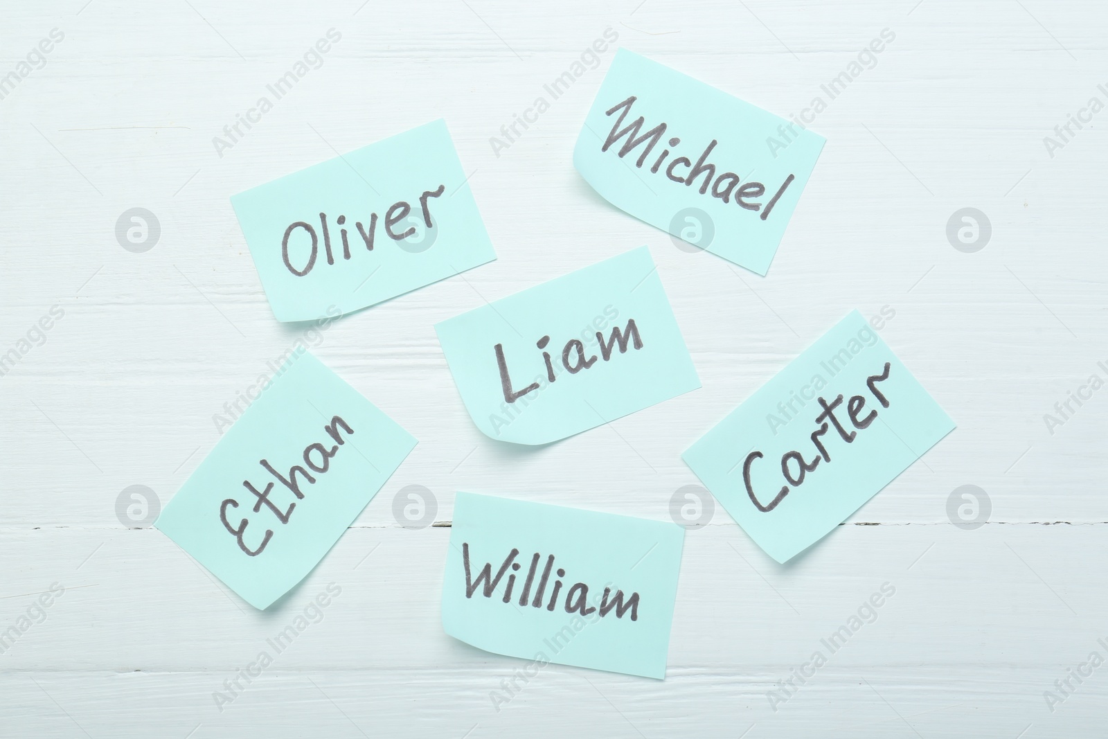 Photo of Paper stickers with different names on white wooden background, flat lay. Choosing baby's name