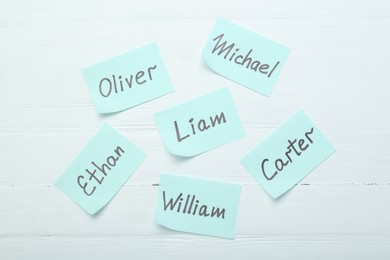Photo of Paper stickers with different names on white wooden background, flat lay. Choosing baby's name