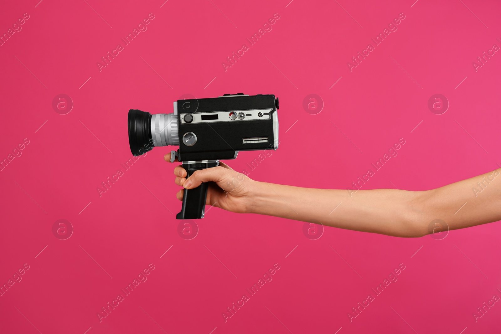 Photo of Woman with vintage video camera on crimson background, closeup of hand