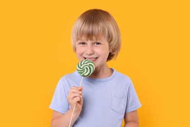 Photo of Happy little boy with lollipop swirl on orange background