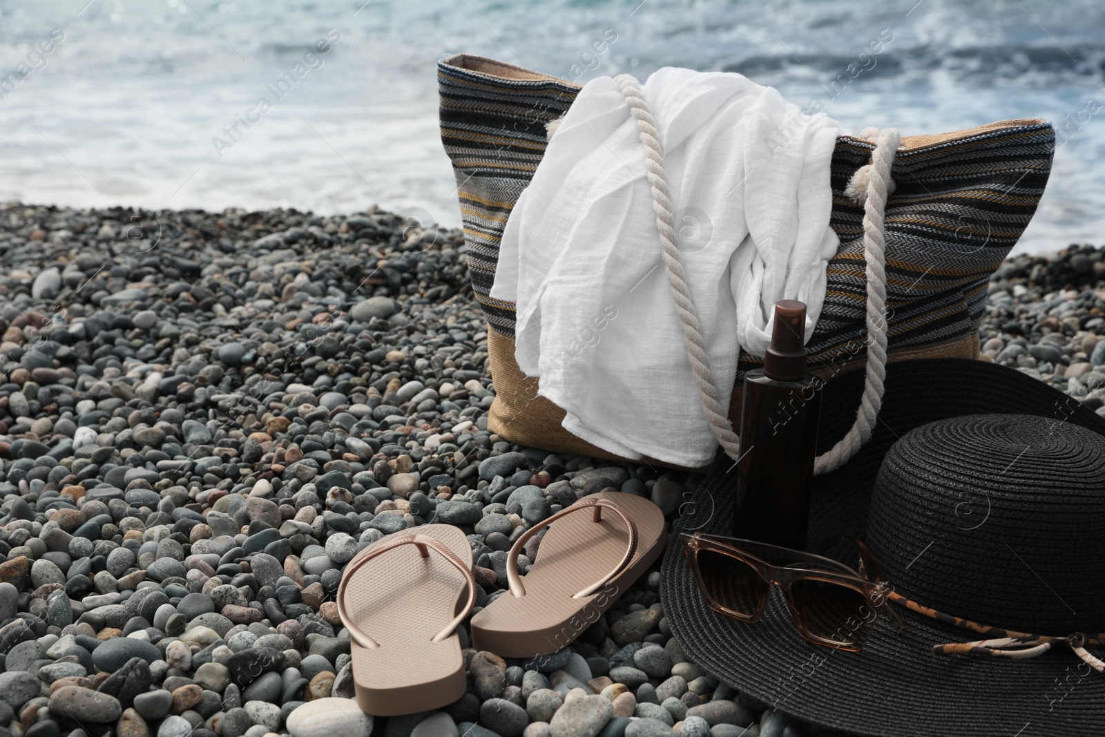 Photo of Beautiful hat with sunglasses, bag and flip flops near sea on pebble beach