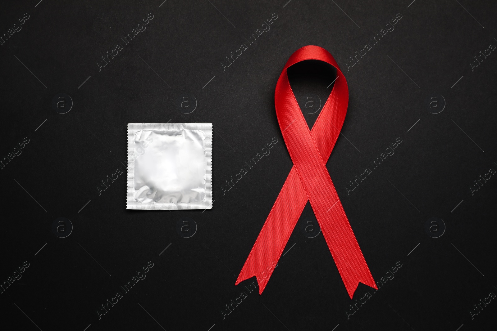 Photo of Red ribbon and condom on black background, flat lay. AIDS disease awareness