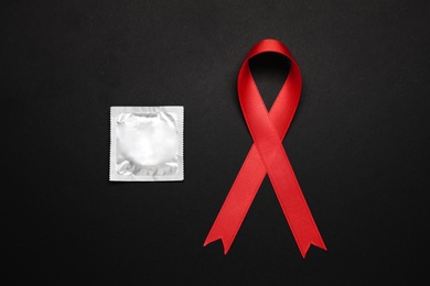 Photo of Red ribbon and condom on black background, flat lay. AIDS disease awareness