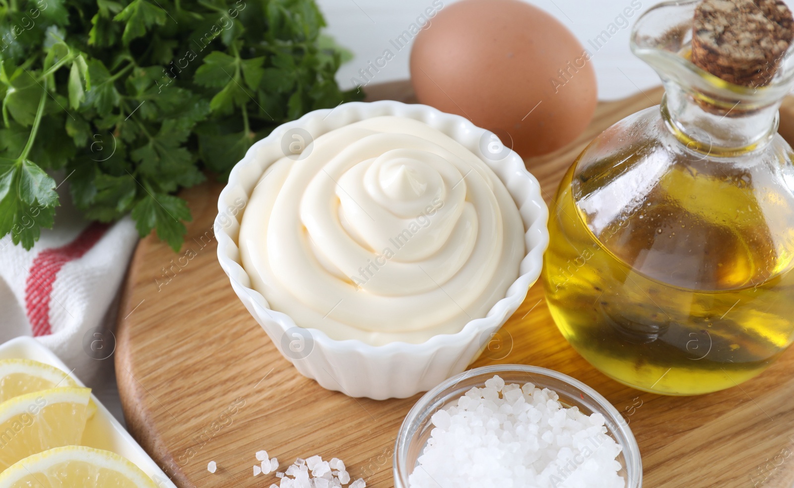 Photo of Fresh mayonnaise sauce in bowl and ingredients on table, closeup