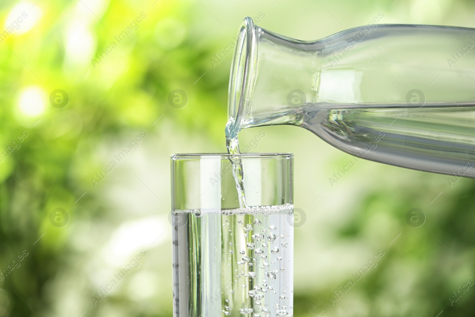 Photo of Pouring water from bottle into glass on blurred background