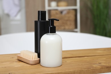 Photo of Wooden bath tray with bottles of shower gels and brush on tub indoors