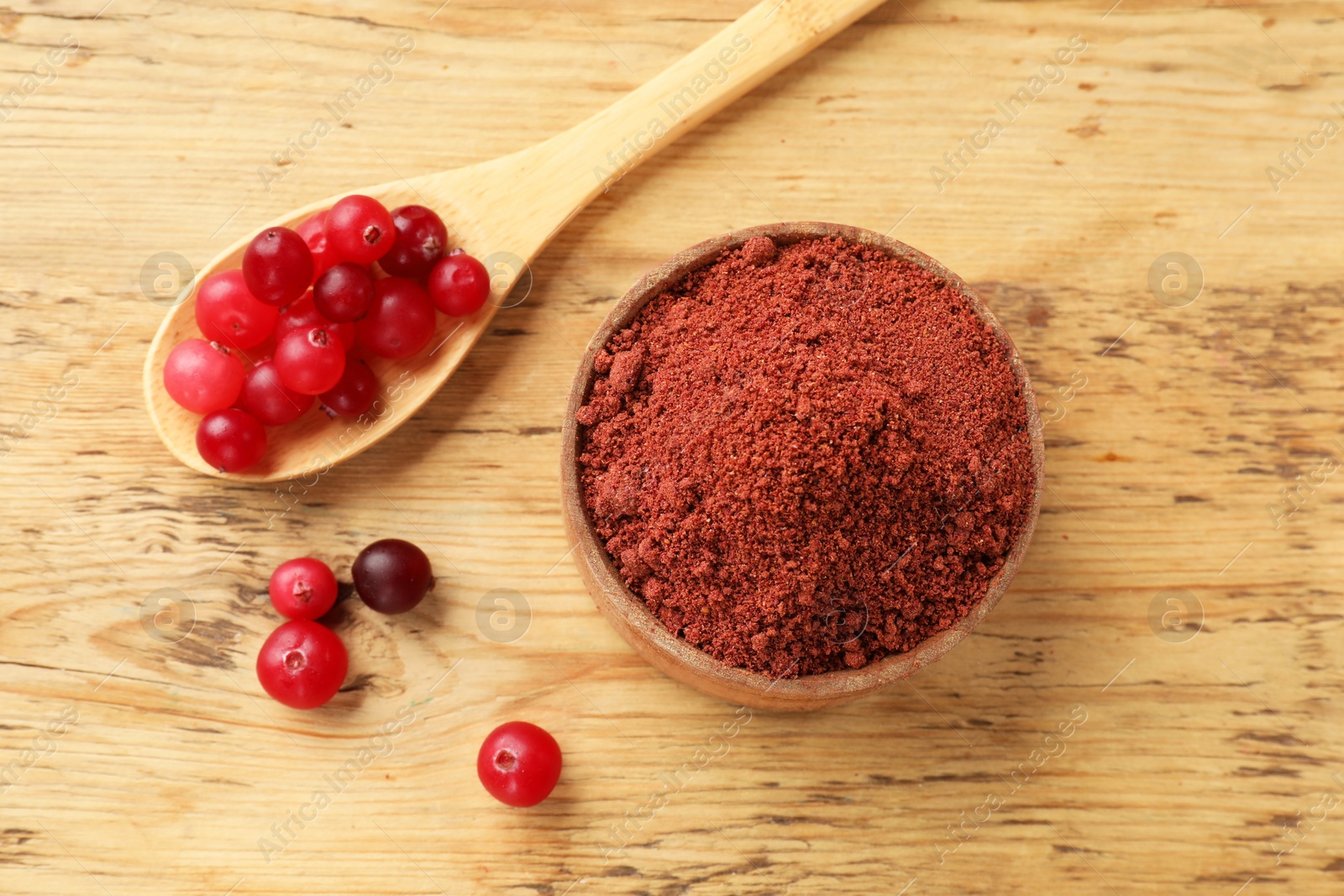 Photo of Cranberry powder in bowl and spoon with fresh berries on wooden table, top view