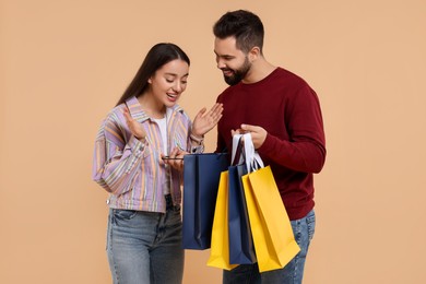Photo of Man showing shopping bag with purchase to his girlfriend on beige background