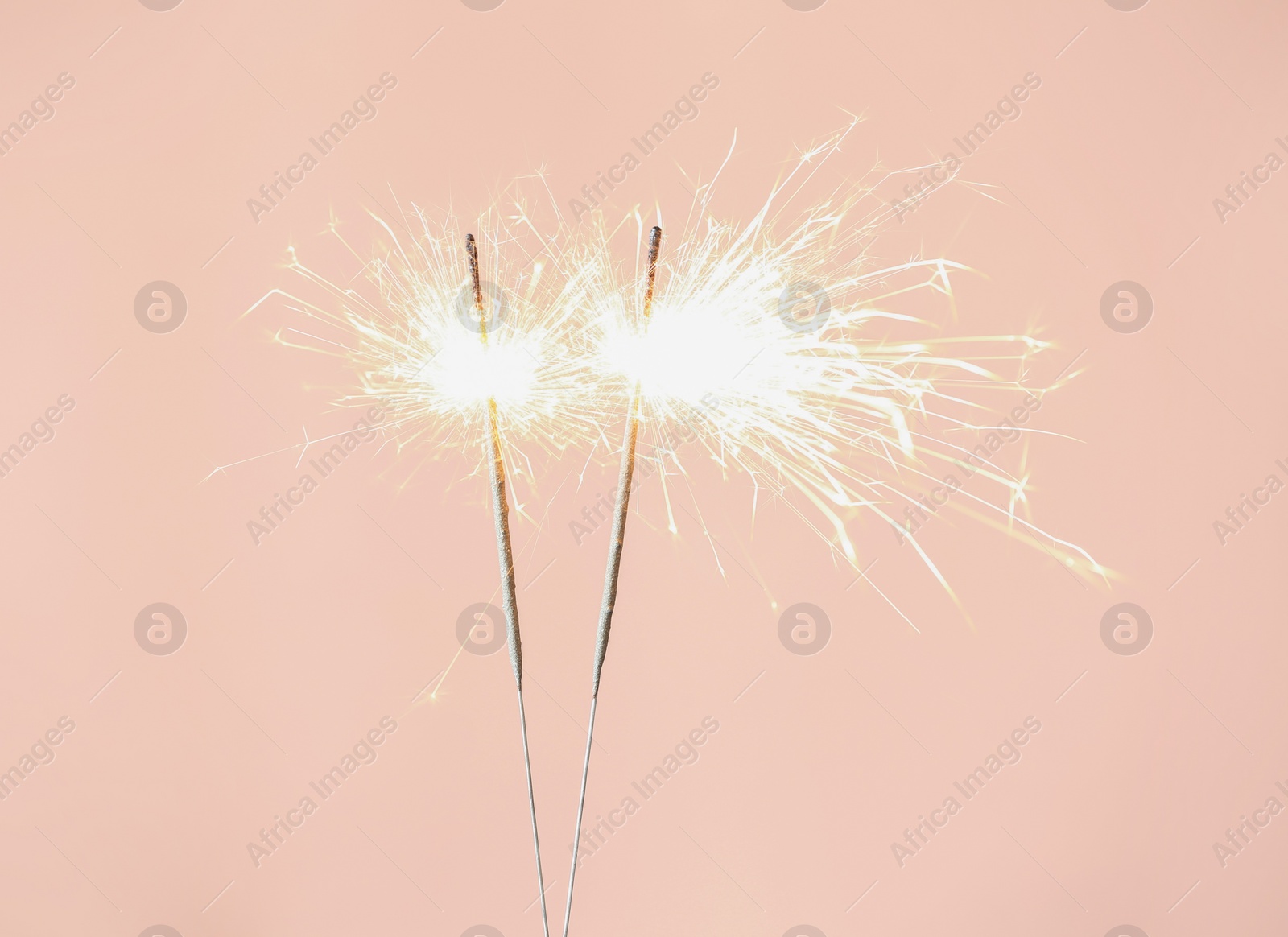 Photo of Bright burning sparklers on pink background, closeup