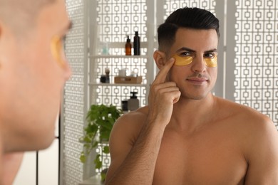Man applying golden under eye patch near mirror at home