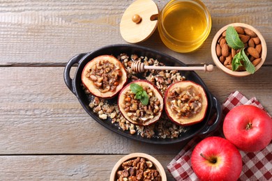 Tasty baked apples with nuts, honey and mint in baking dish on wooden table, flat lay. Space for text