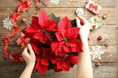 Photo of Woman with poinsettia (traditional Christmas flower) at wooden table, top view