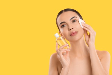 Photo of Beautiful woman removing makeup with cotton pad on yellow background, space for text