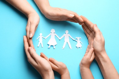 Parents and child protecting paper cutout of family on light blue background, top view