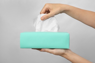 Photo of Woman taking paper tissue from box on light background, closeup