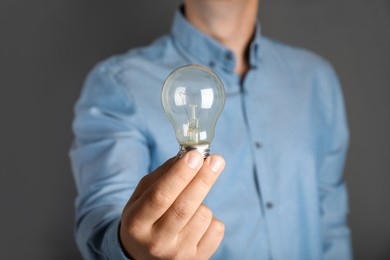 Photo of Man holding incandescent light bulb on grey background, closeup