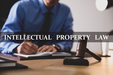 Image of Intellectual property law. Jurist working at table in office, focus on gavel