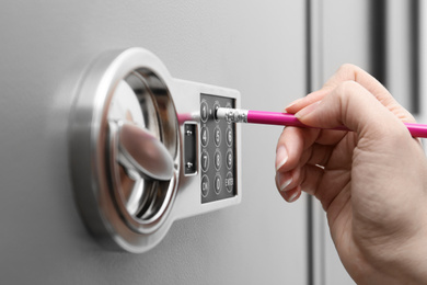 Photo of Woman using pencil to enter code on keypad of modern safe, closeup