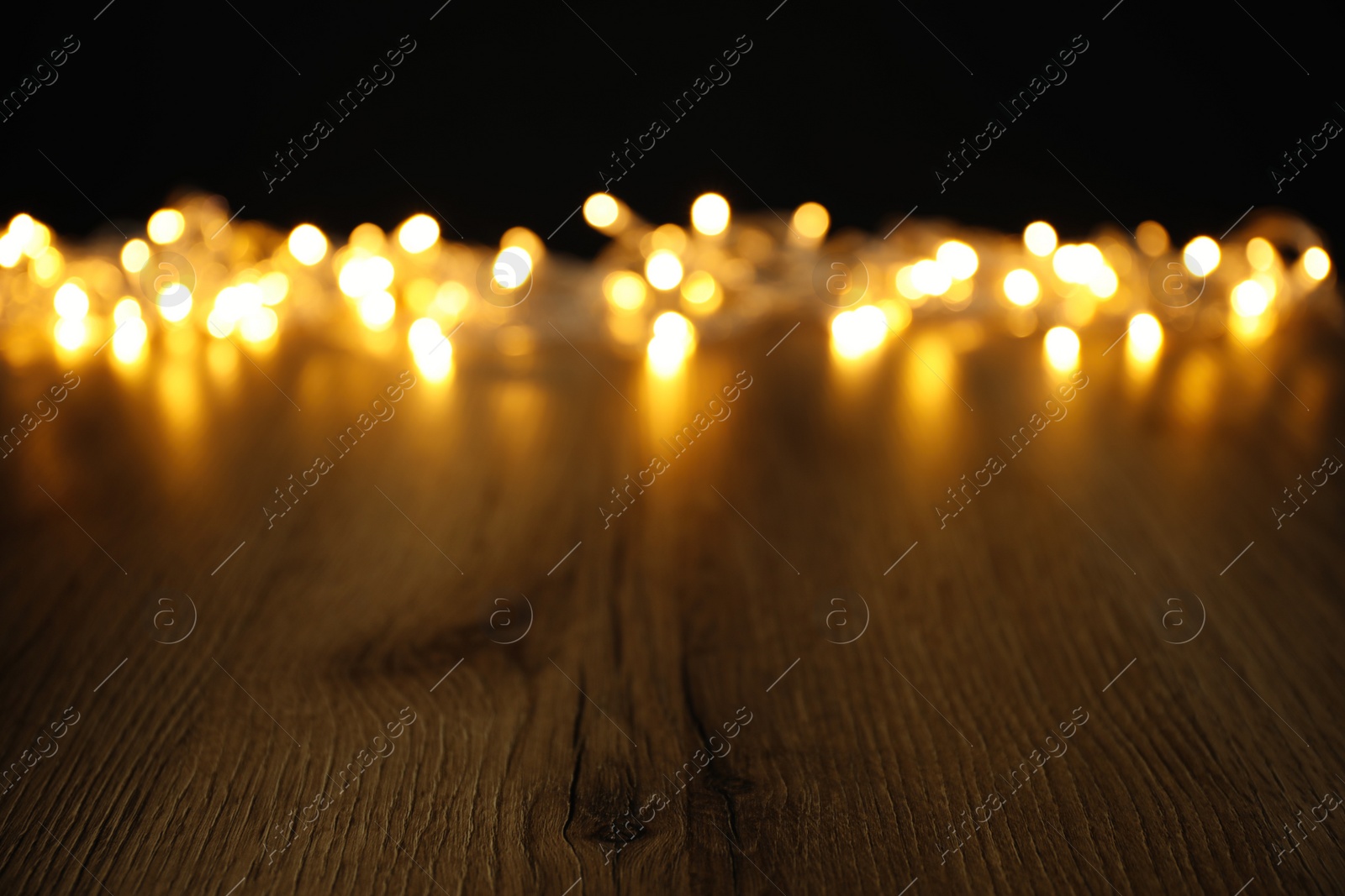 Photo of Blurred view beautiful glowing lights, focus on wooden table. Space for text