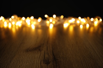 Blurred view beautiful glowing lights, focus on wooden table. Space for text