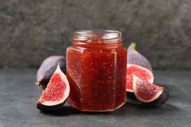 Photo of Glass jar with tasty sweet jam and fresh figs on grey table, closeup